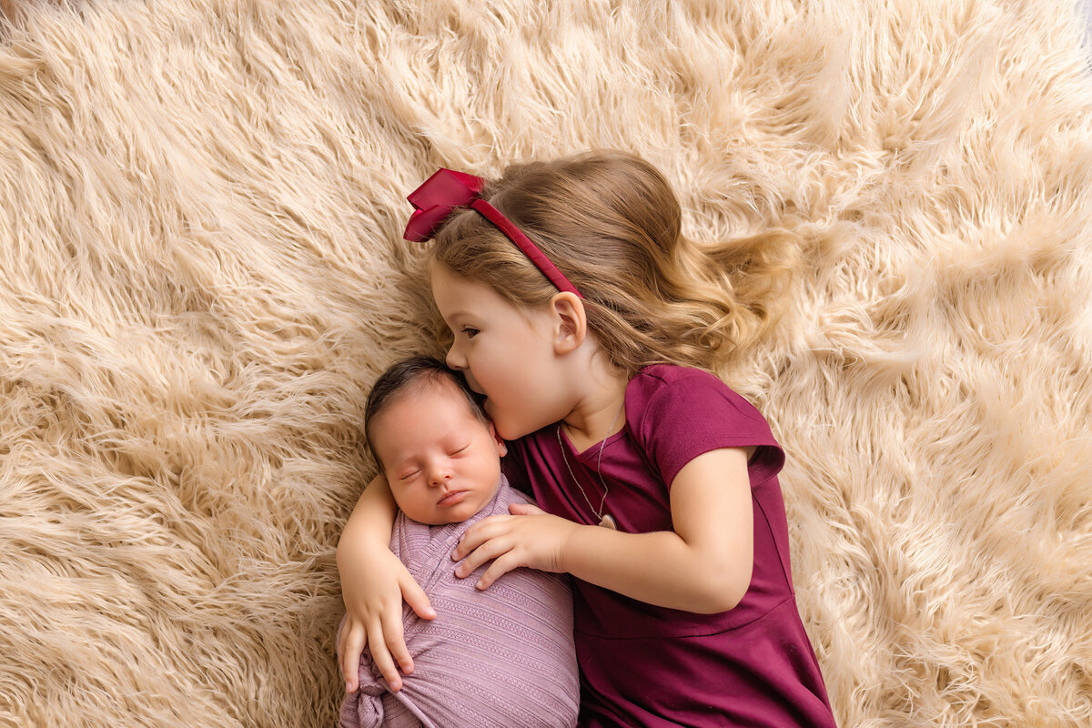 Newborn Photographer, a newborn baby is cuddled by her older sister