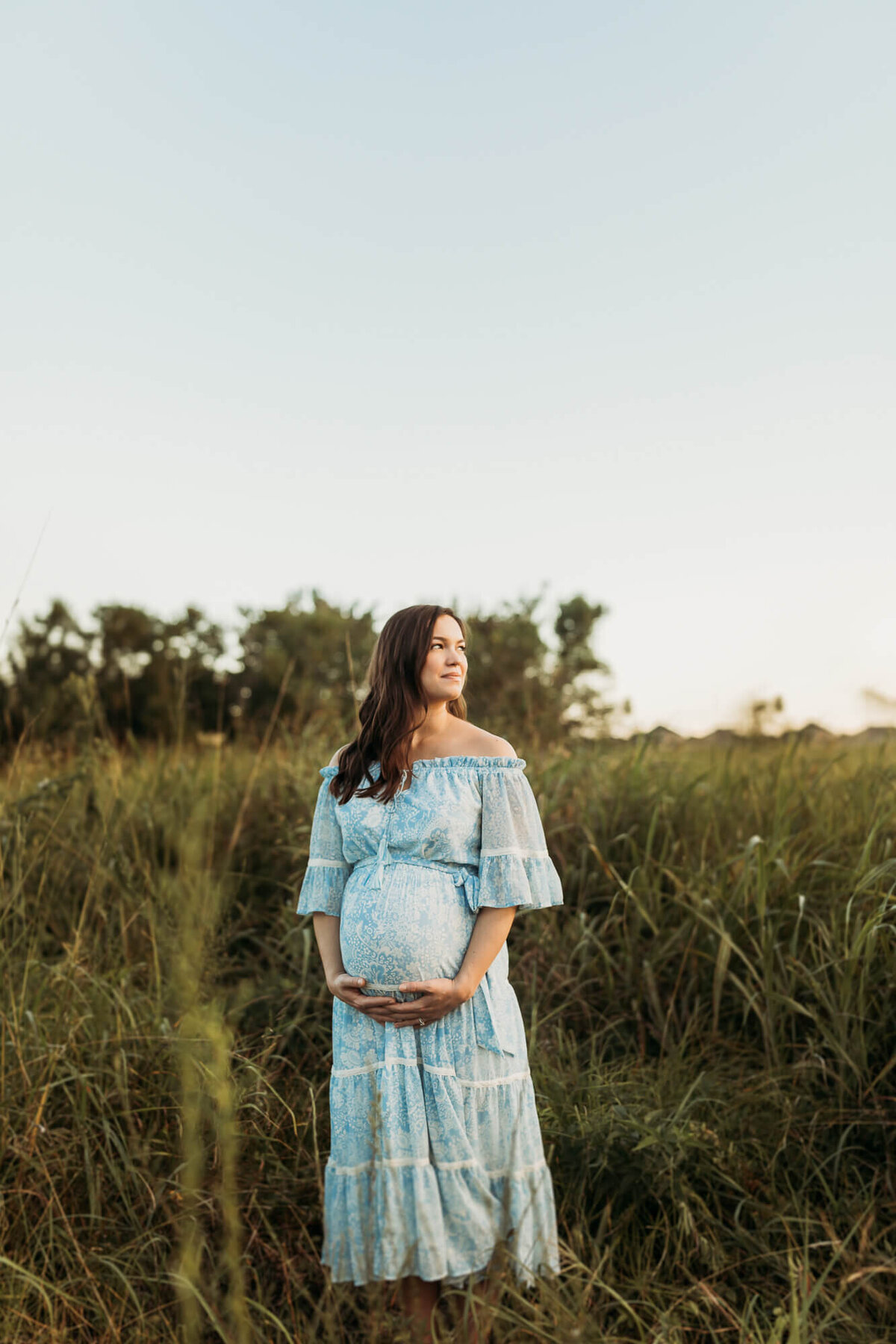 gorgeous woman daydreaming about her son and caressing her belly while standing in overgrown grass field.