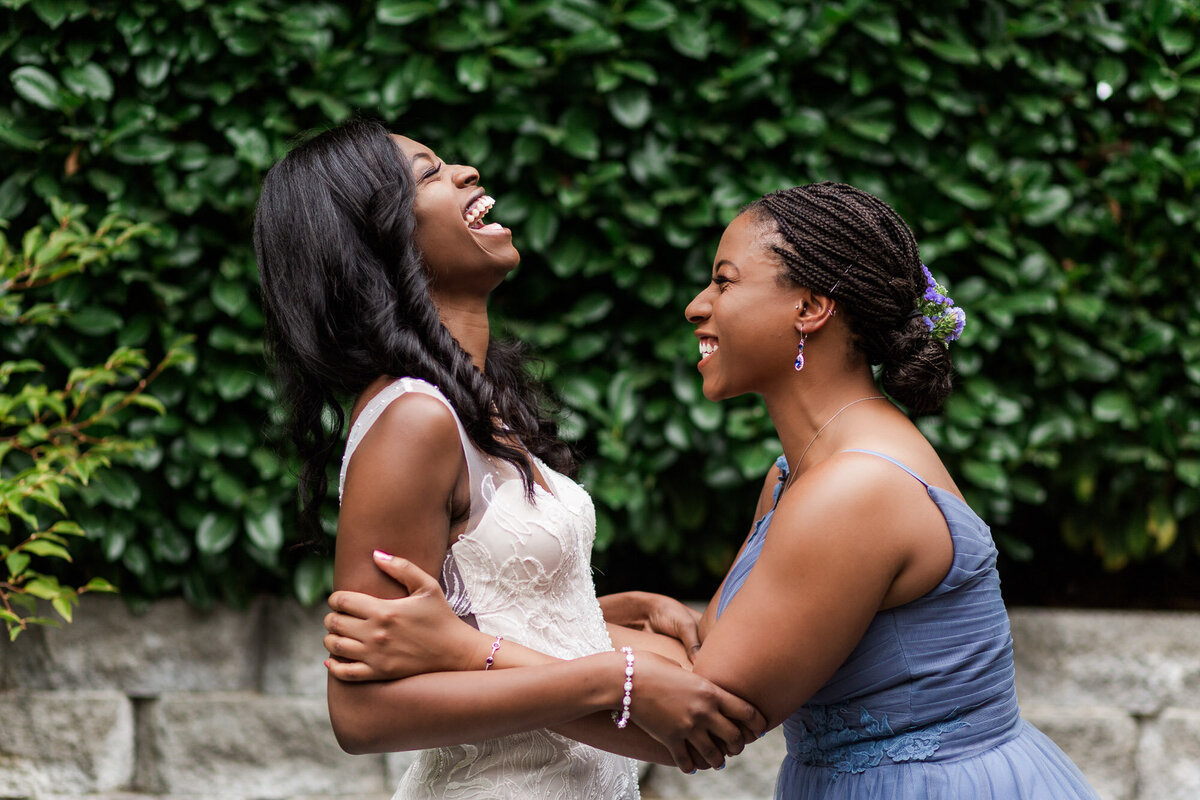 Bride-and-bridesmaid-laugh-as-they-get-ready-for-wedding-at-beautiful-outdoor-wedding-venue-Green-Gates-at-Flowing-Lake-in-Snohomish-WA-photo-by-Joanna-Monger-Photography