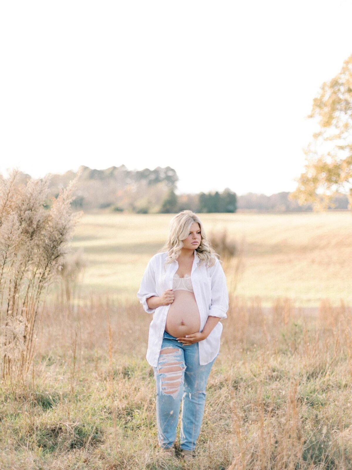 Woman stands in grass field holding bare pregnant belly.