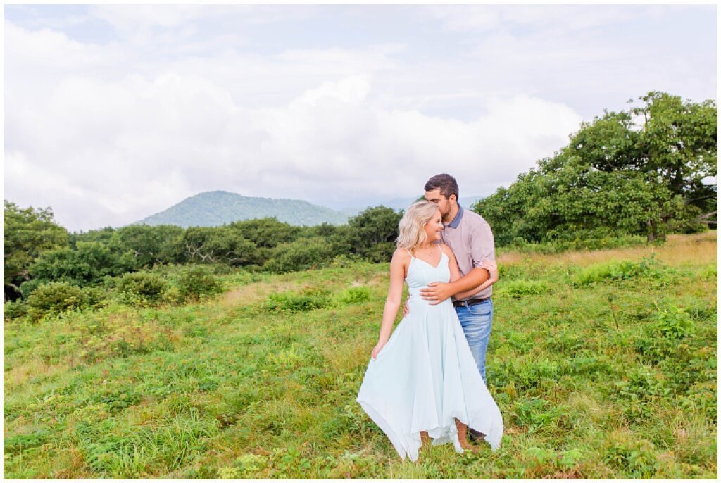 engaged couple kissing in field with mountains in the background