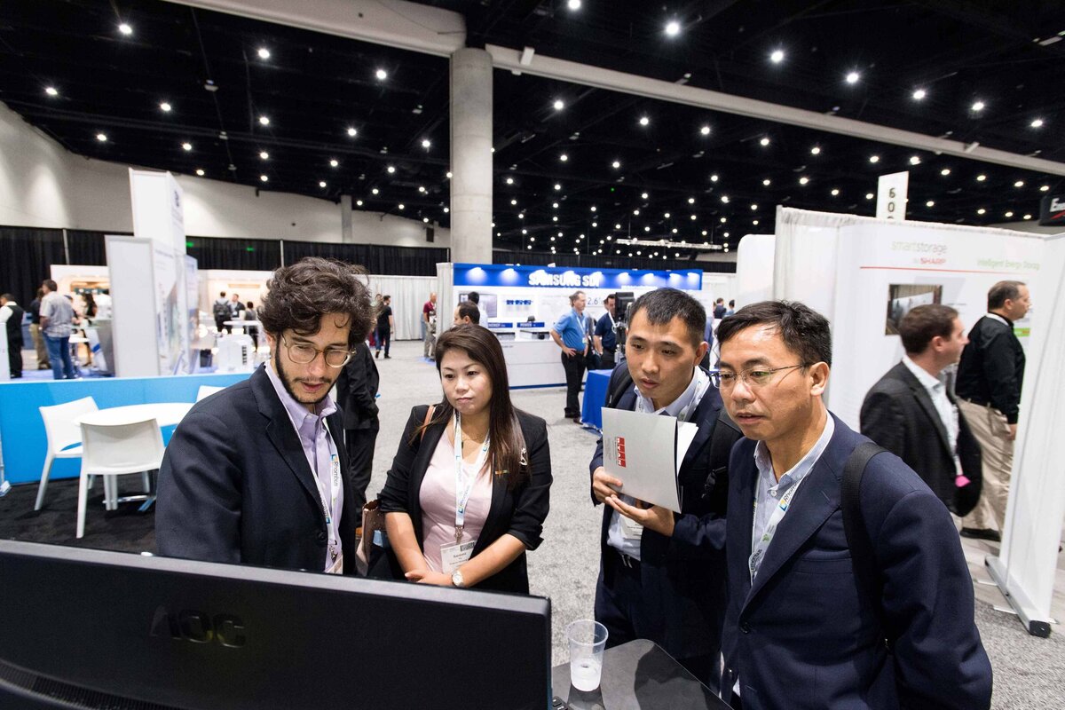 A group of 4 people crow around a monitor staring at the screen to learn about the product being promoted during trade show in San Diego