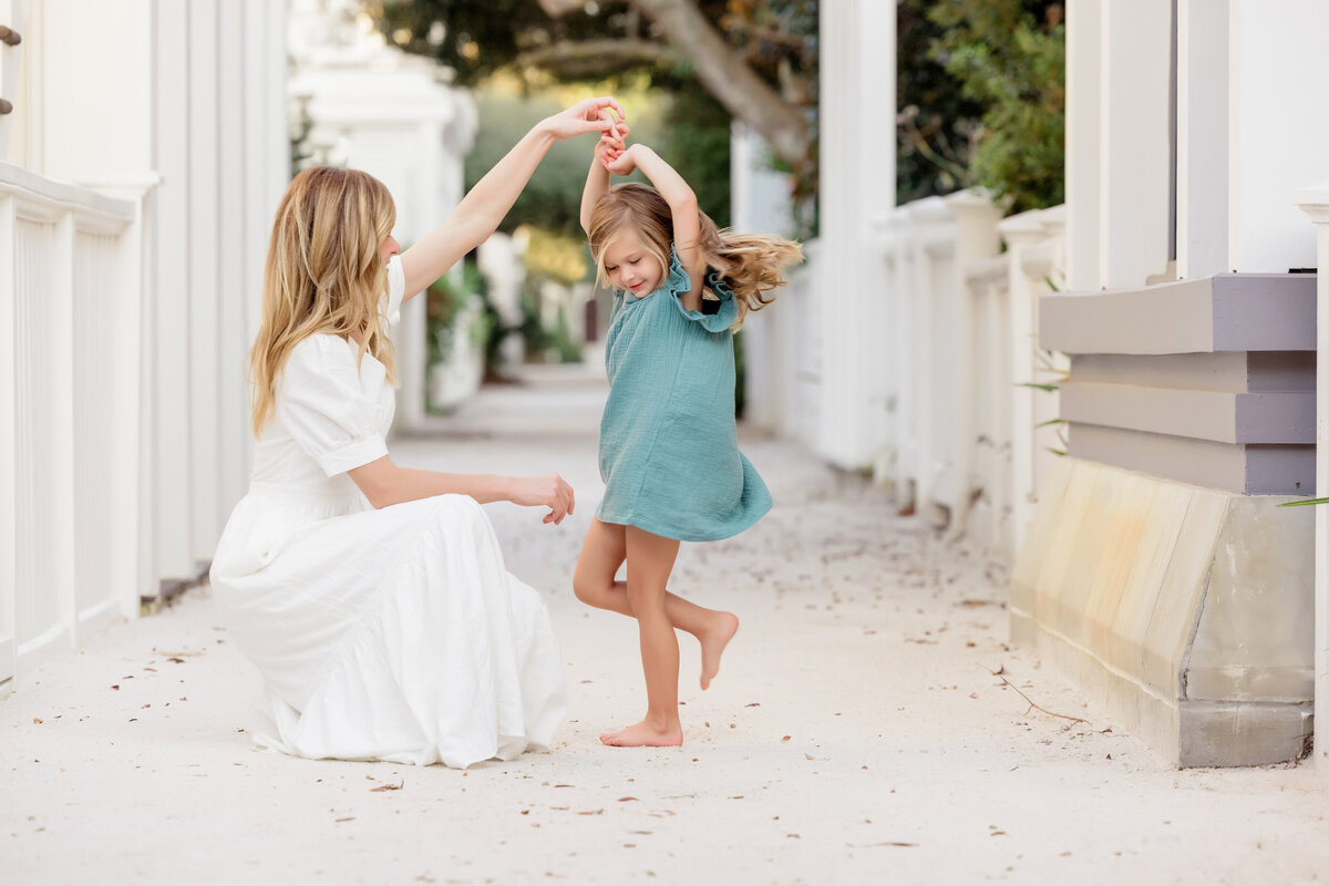 A mom crouched down dancing with a small girl