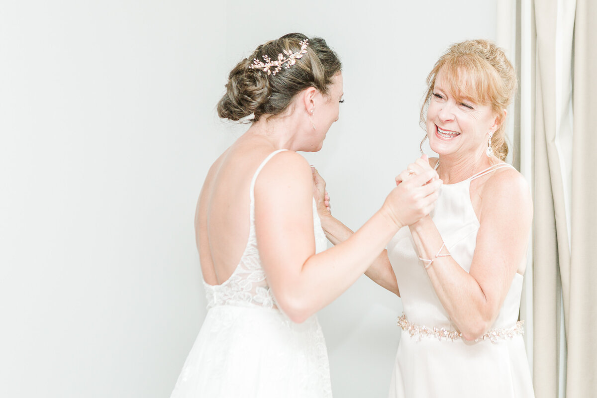 Bride and her mother share a first look before her Ocean View of Nahant wedding in MA. They are holding hands and laughing. Captured by Lia Rose Weddings