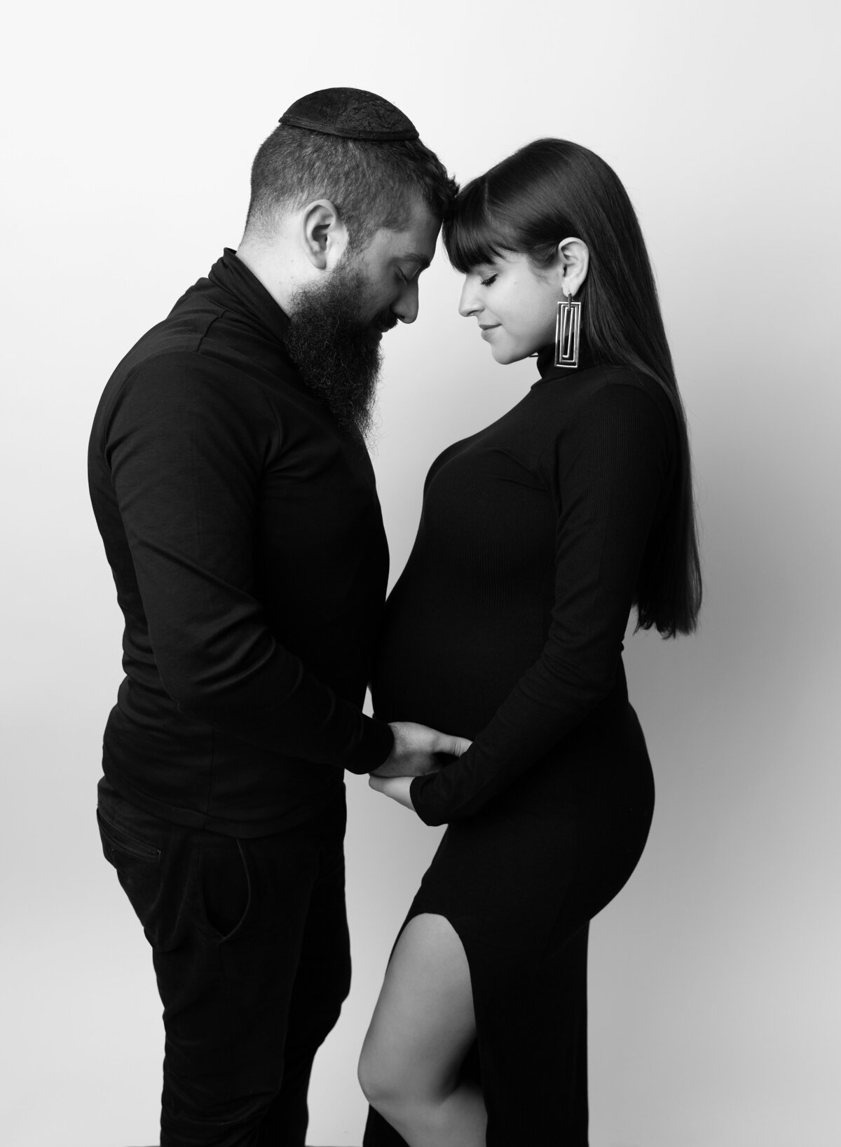 Expectant mom and husband stand face-to-face for Brooklyn, NY maternity photos. Mom and Dad's heads are touching and both mom and dad's hands are resting on the baby bump.