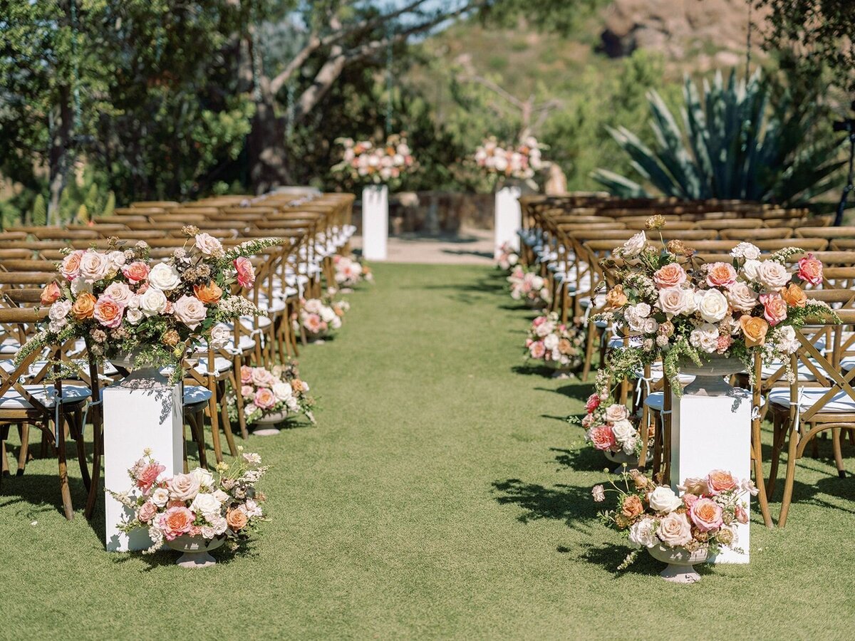 Bright big flowers line the wedding aisle with inviting bouquets at the entrance leading up to a wedding arbor.