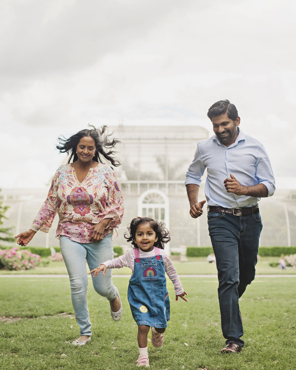 A mother and father run after their smiling little girl at Kew Gardens in Surrey