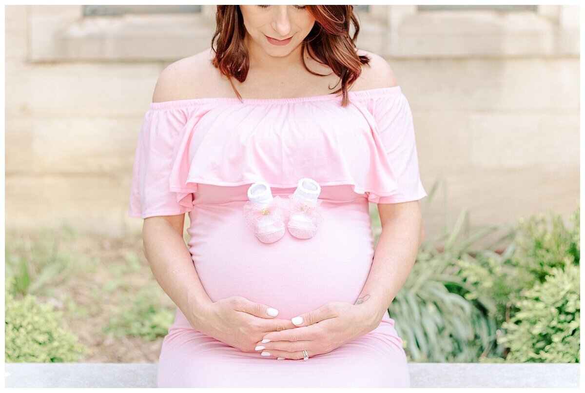 Maternity Photography in Wexford taken outdoors.  the mom is sitting and looking at her baby belly and has tiny shoes on her belly
