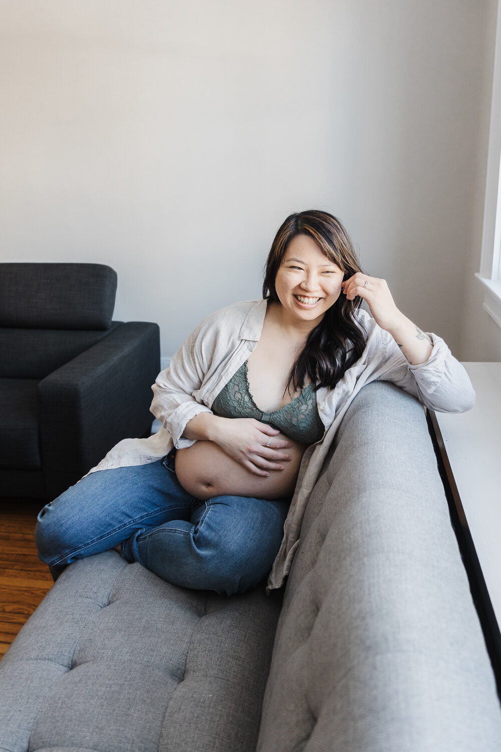 Pregnant Asian woman on grey living room couch