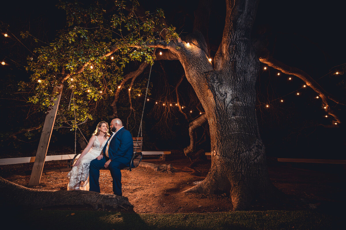 Bride and groom on swinging chair under string lights at Southern California wedding