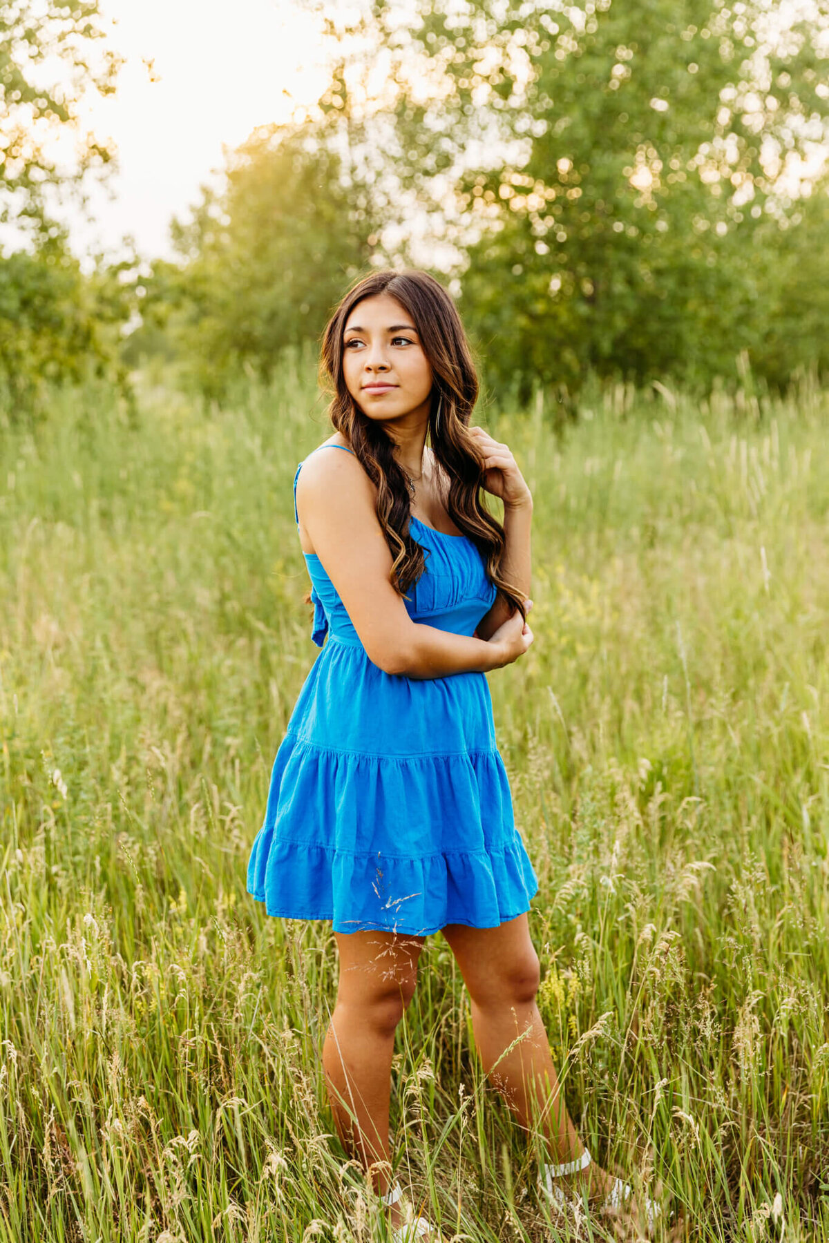 beautiful teenage girl in a bright blue dress playing with hair as she looks into the field