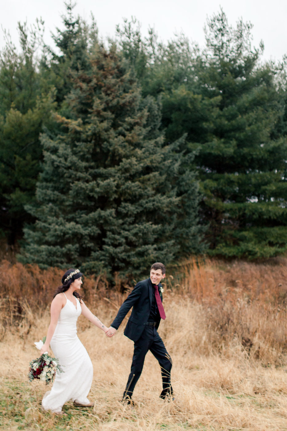 couple walks through field and spruce trees rochester minnesota elopement