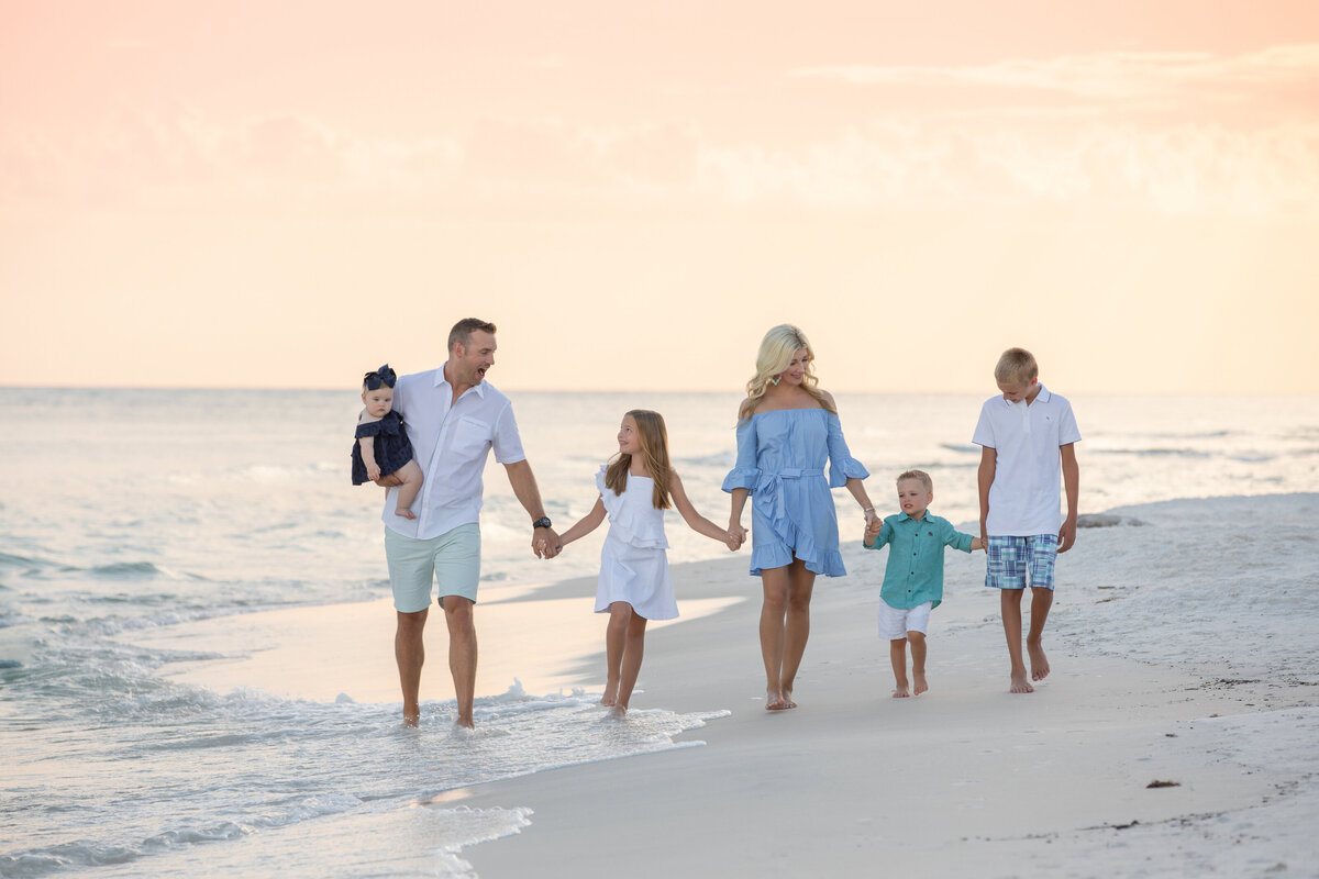 A family holding hands with their arms out walking along the beach