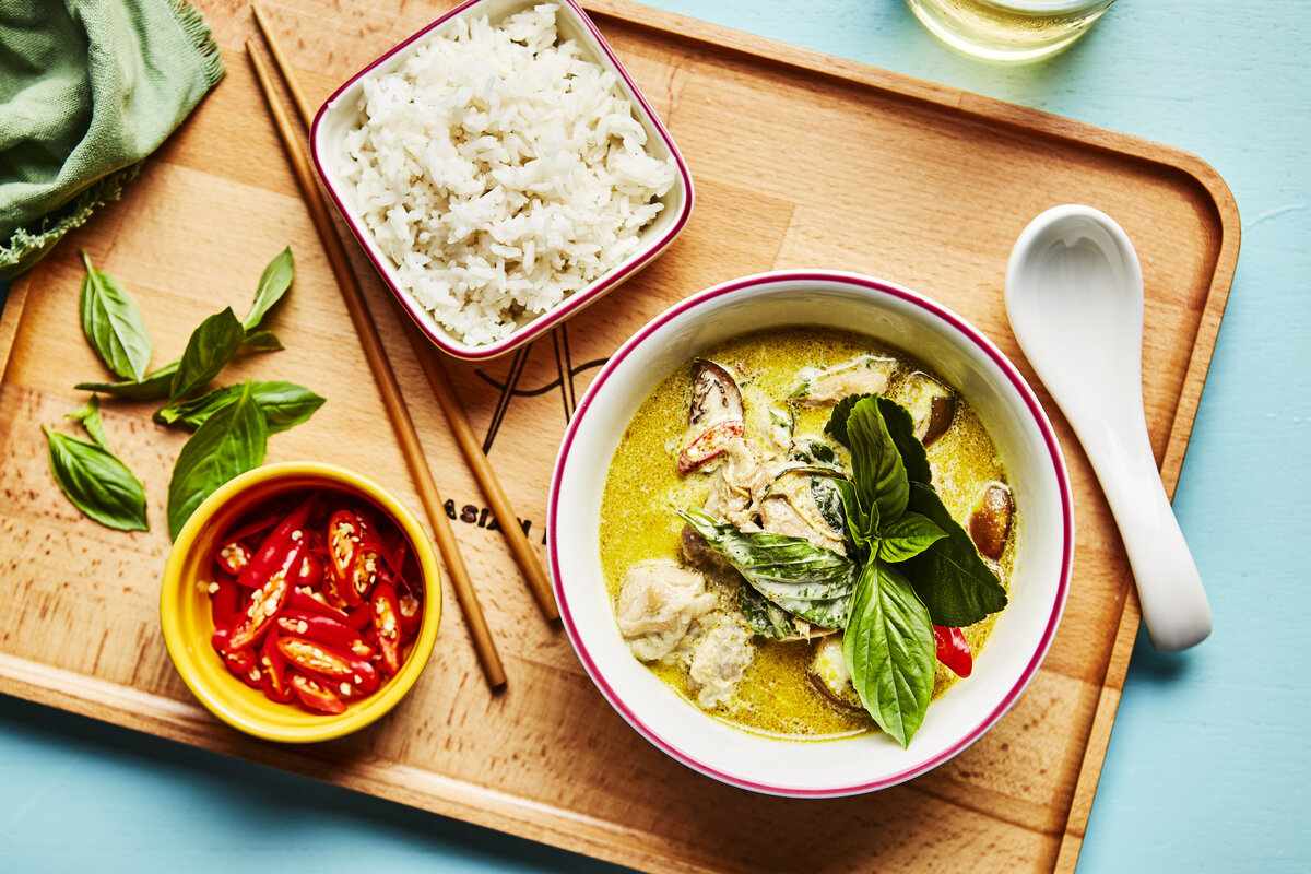 A bowl of thai green curry with rice and peppers next to it.