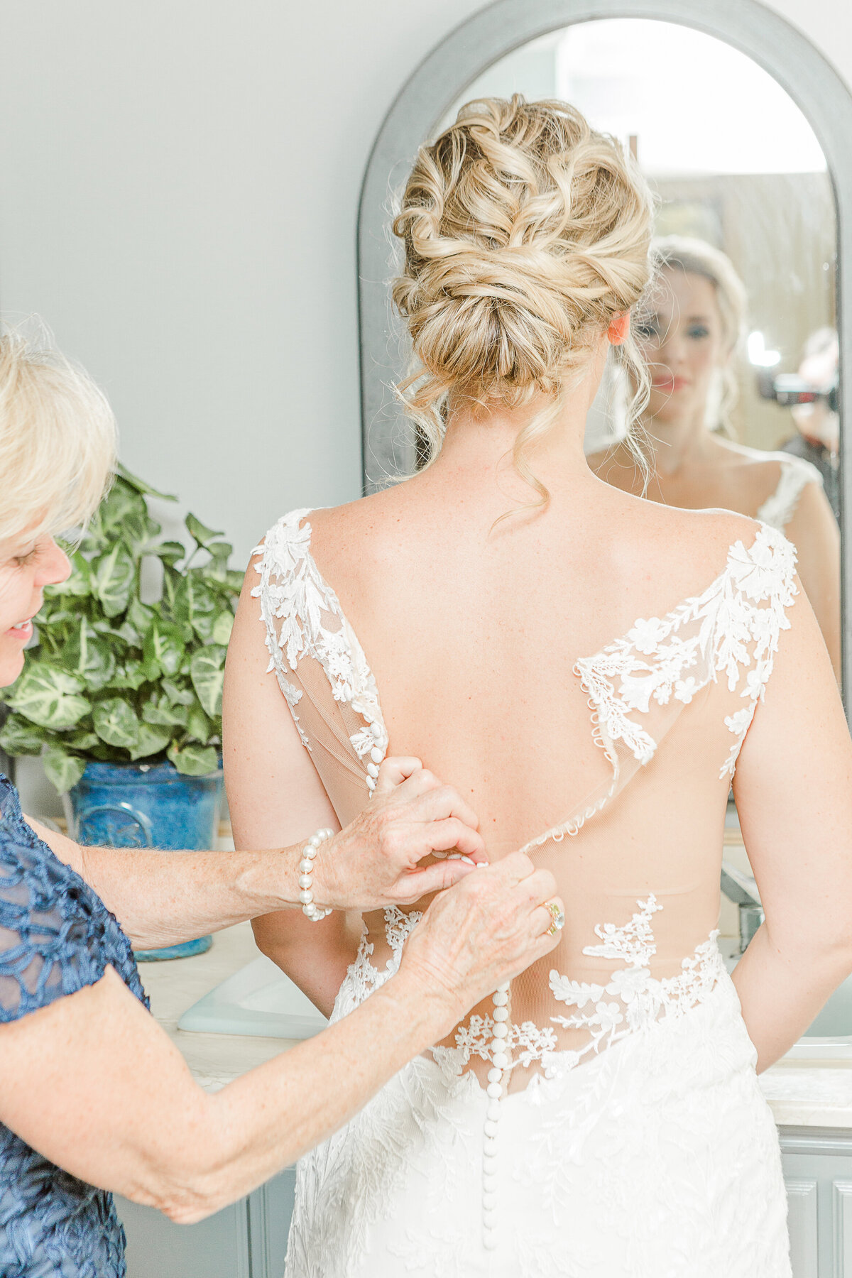 Mother of the bride helps her daughter fasten her wedding gown.