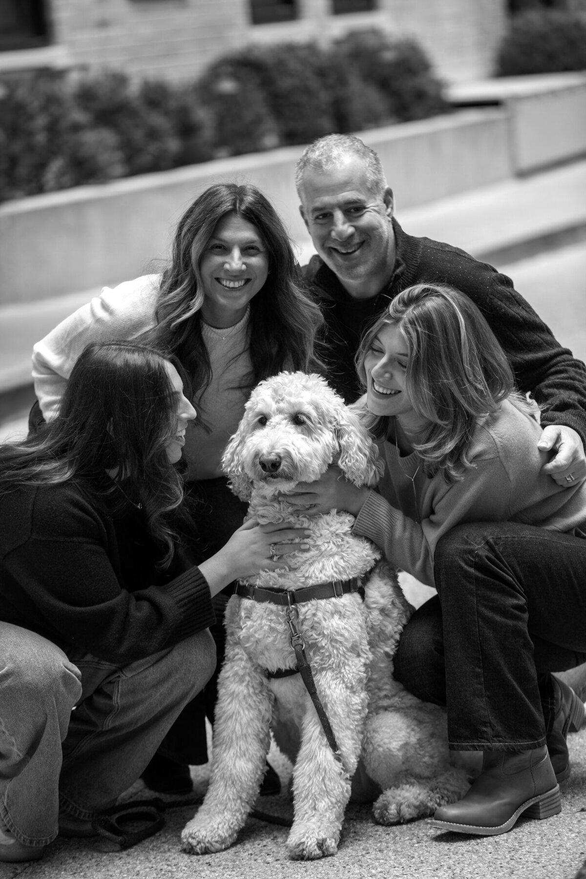 Black and white photo of a white dog surrounded by two college-aged daughters and parents New York City Upper East Side photographer Milestone Images
