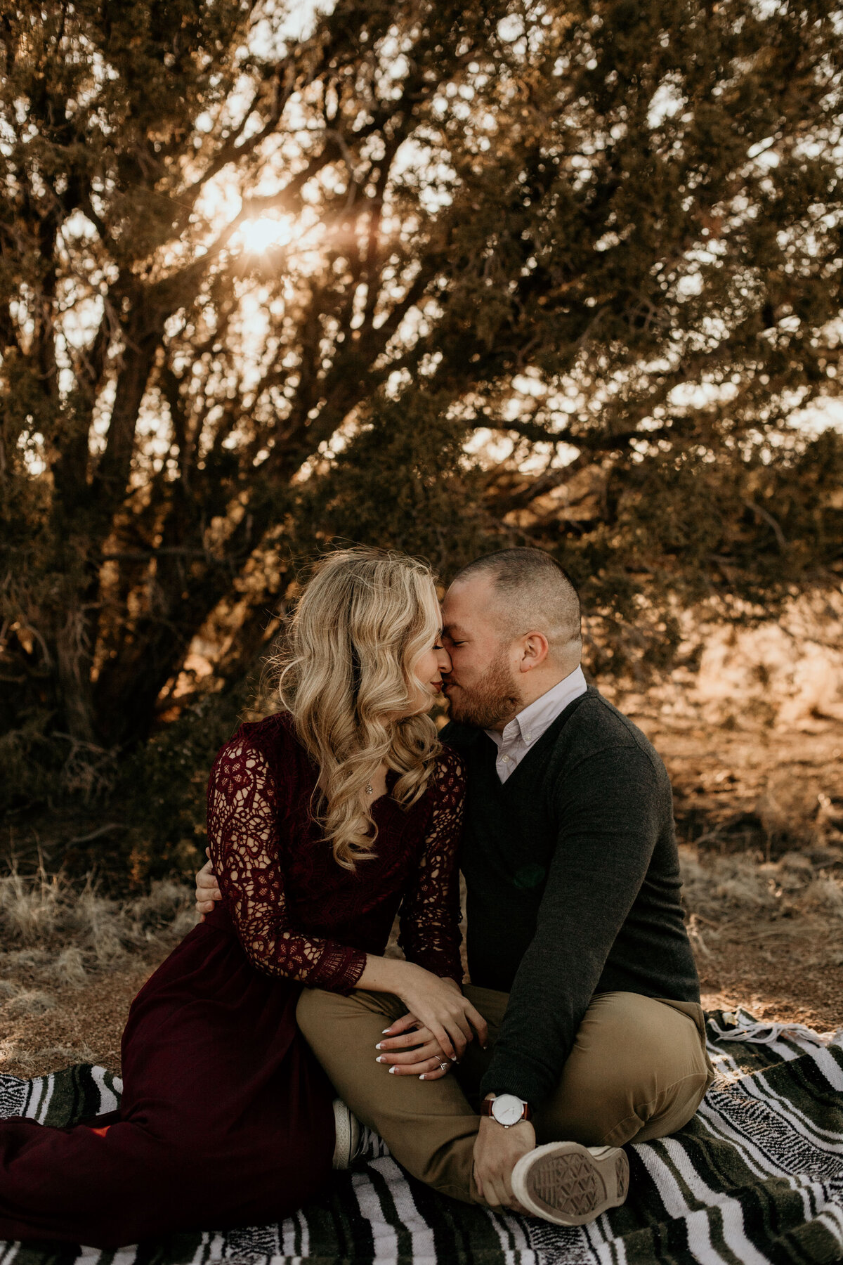 man sitting on a blanket with fiancé kissing her