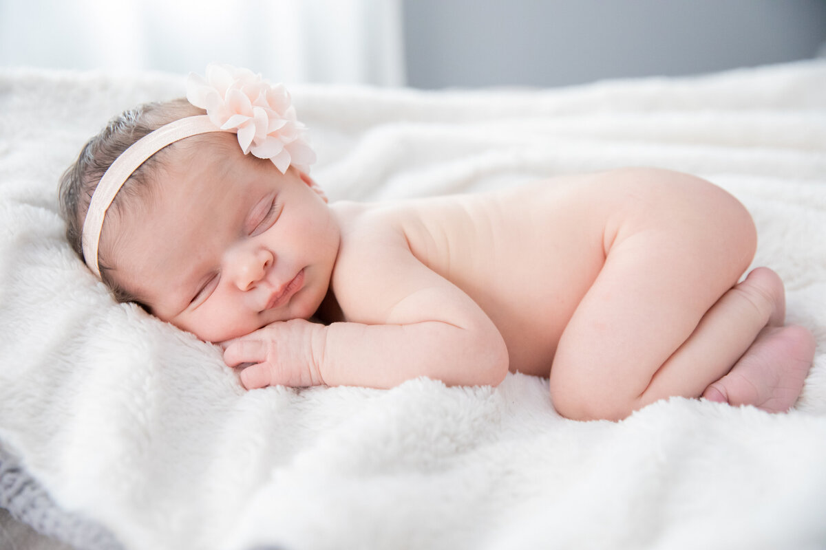 A naked baby girl in a bow sleeps curled up in a newborn photo session Nyack baby photographer Milestone Images