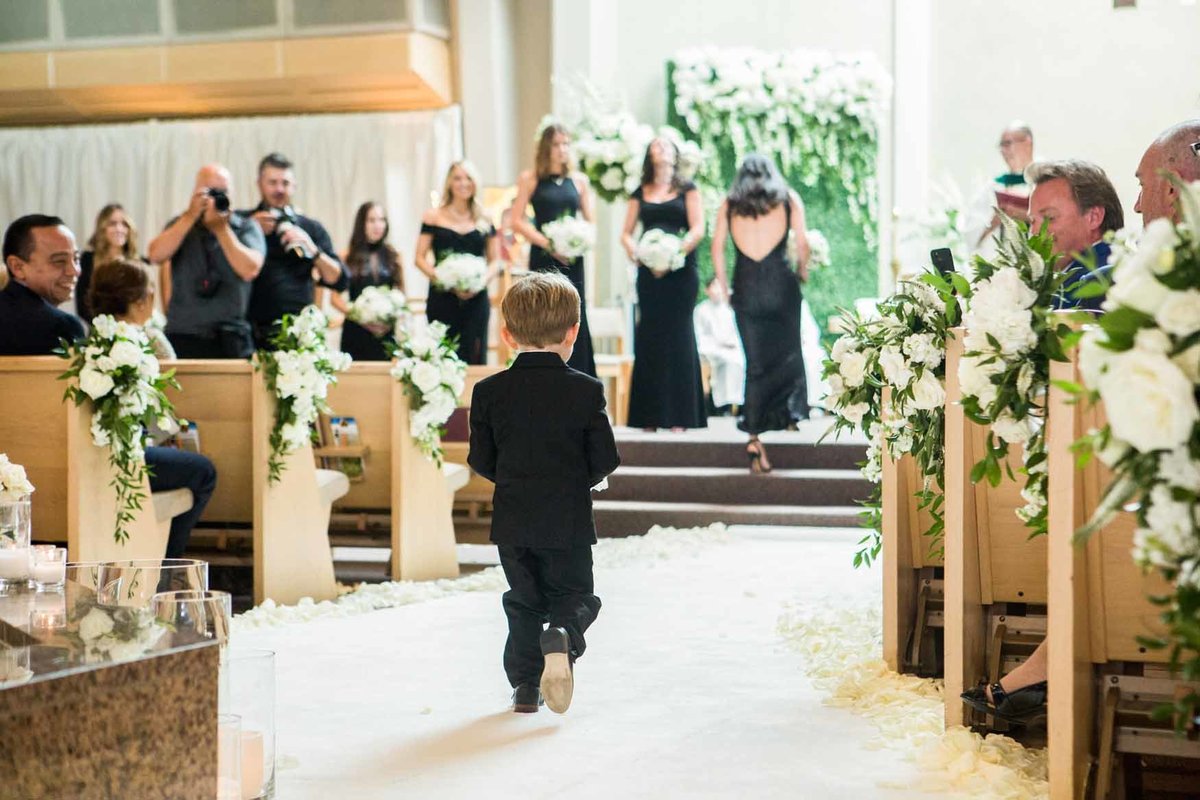Ring bearer walks up aisle with white rose petals