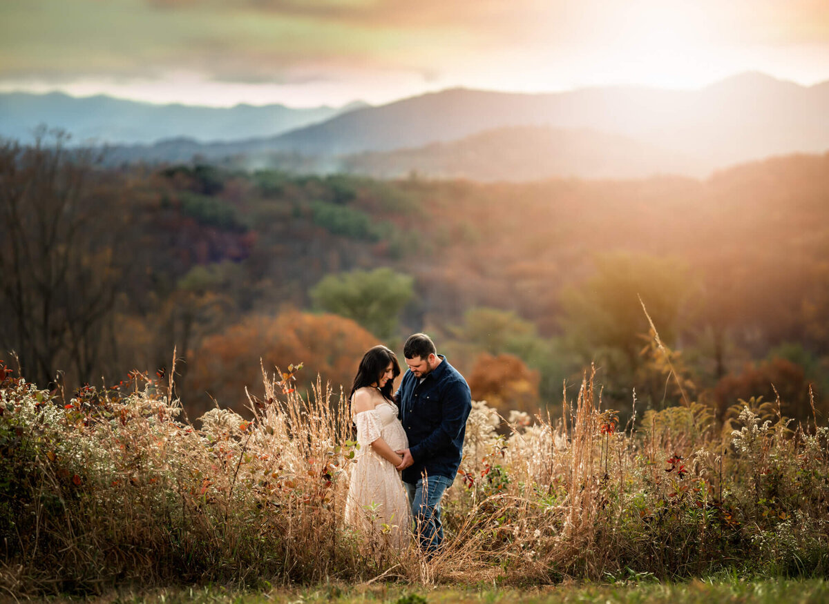 Beautiful mountains surround a couple who cradle their baby bump near Asheville NC