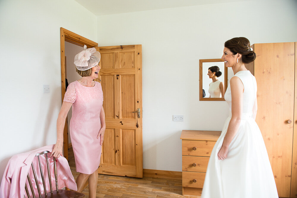 mother of the bride wearing pink and a birdcage headpiece looking at her daughter, wearing a vintage, tea length wedding dress