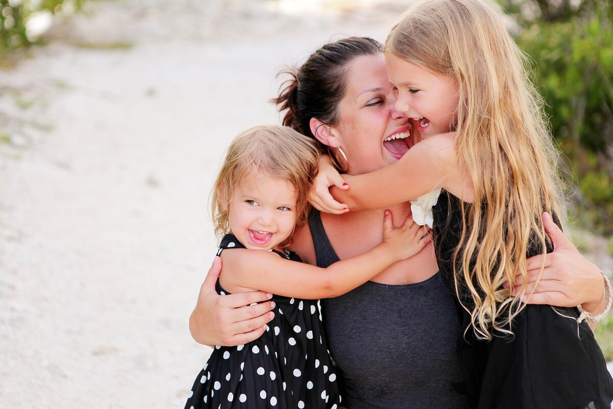 A mom hugging and laughing with her two daughters on Honeymoon Island FL.