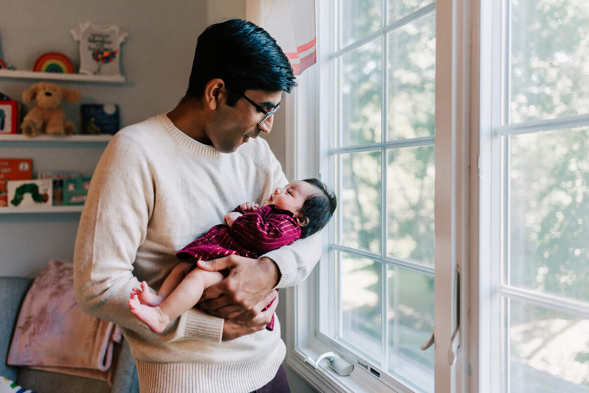 man holding baby girl by a big window
