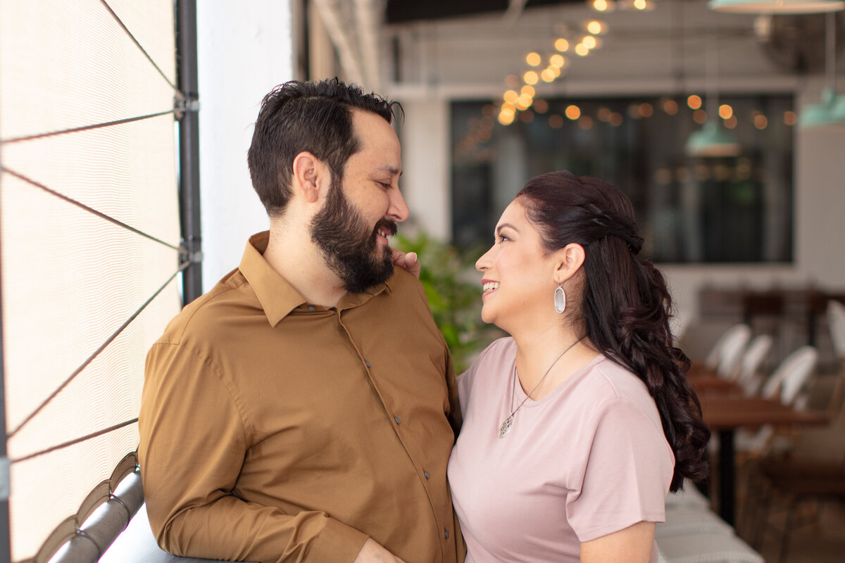 couple stand in window light downtown San Antonio brown shirt pink dress by Texas wedding photographer