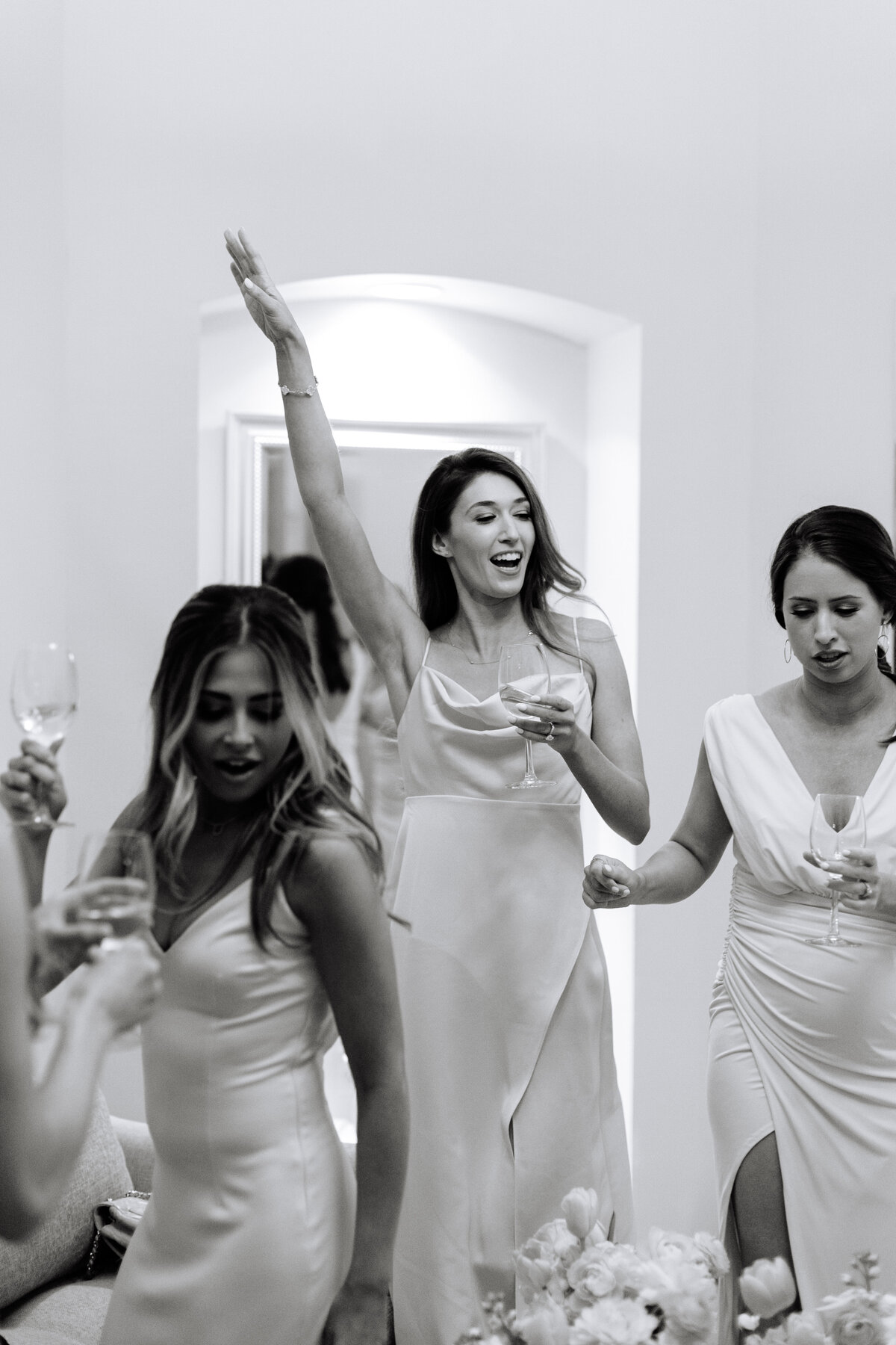 black and white image of bridesmaids dancing with bride with champagne in hand.