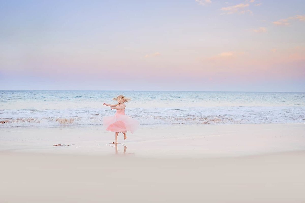 Young girl in pink dress twirls on the sand at the beach  in Wailea