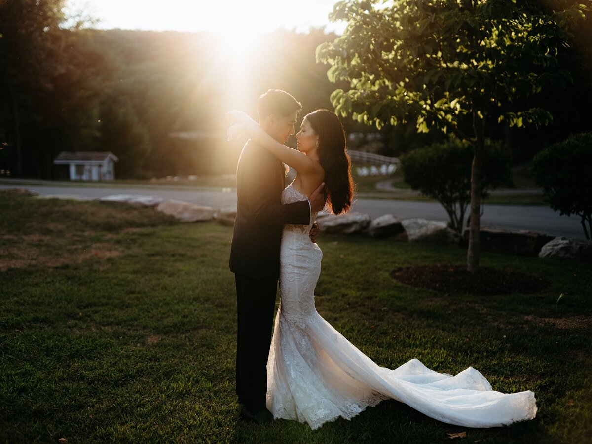 Dramatic sunlit portrait of stylish bride and groom embracing outside the wedding reception at Cedar Lakes Estate in the Catskills