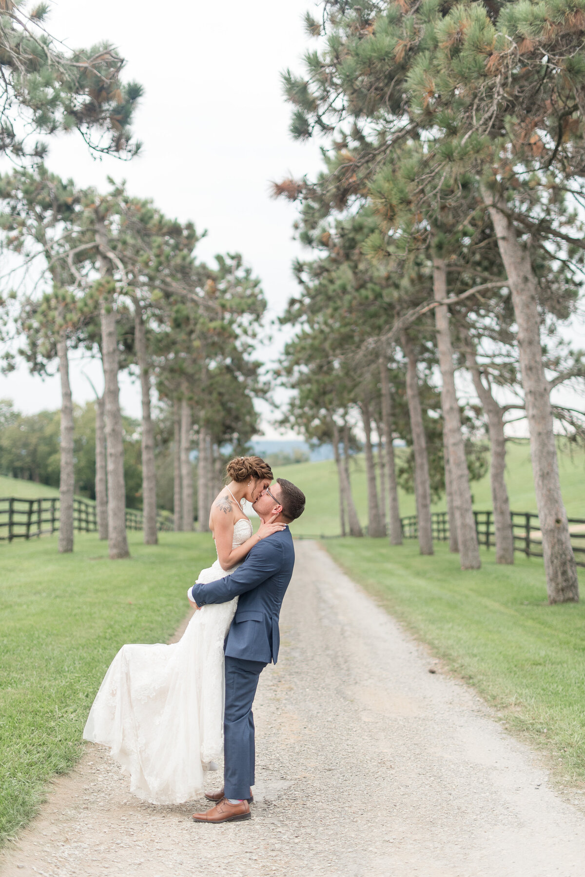 Groom lifting Bride off the ground as they kiss on tree-lined pathway at Lauxmont Farms.