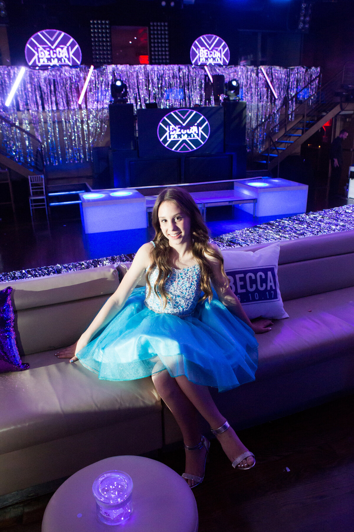 A girl in a blue dress poses in her purple decorated room bat mitzvah New York City bar photographer Milestone Images