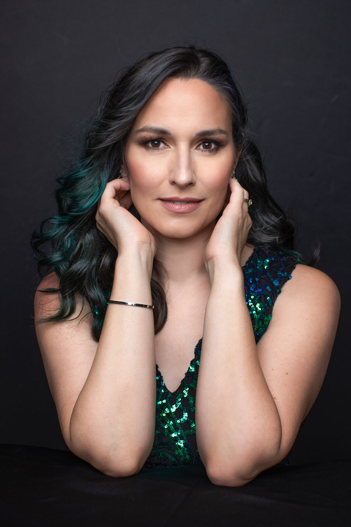 A woman with dark brown hair and green hair along with a green dress lightly touches her face as she poses for a portrait for Janel Lee Photography studios Cincinnati Ohio