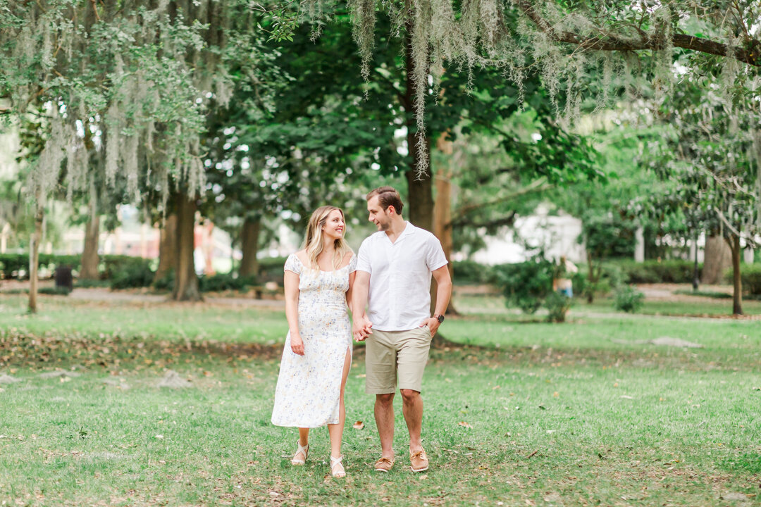 A Couple holds hands while walking in Forsyth Park. Captured by Arkansas Wedding Photographer, Photography by Karla.