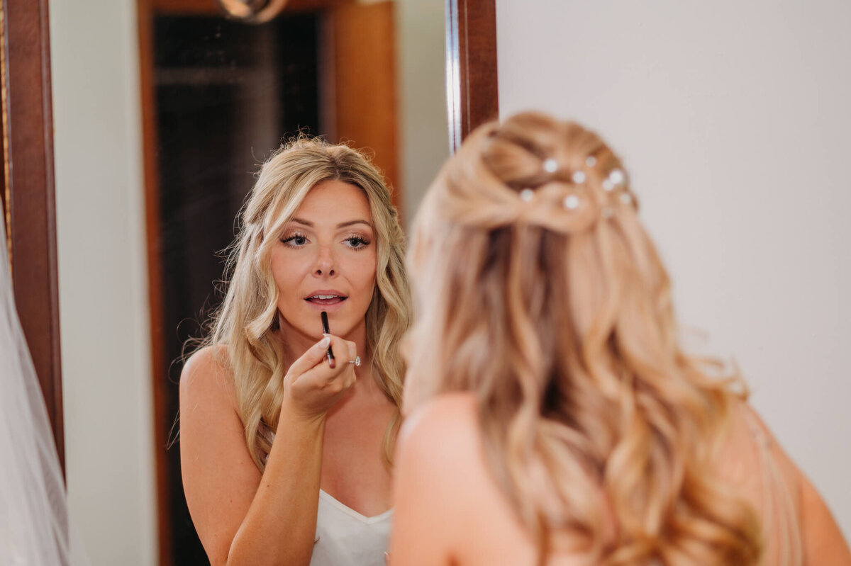 Photo of a woman standing in front of a mirror and putting on lipstick