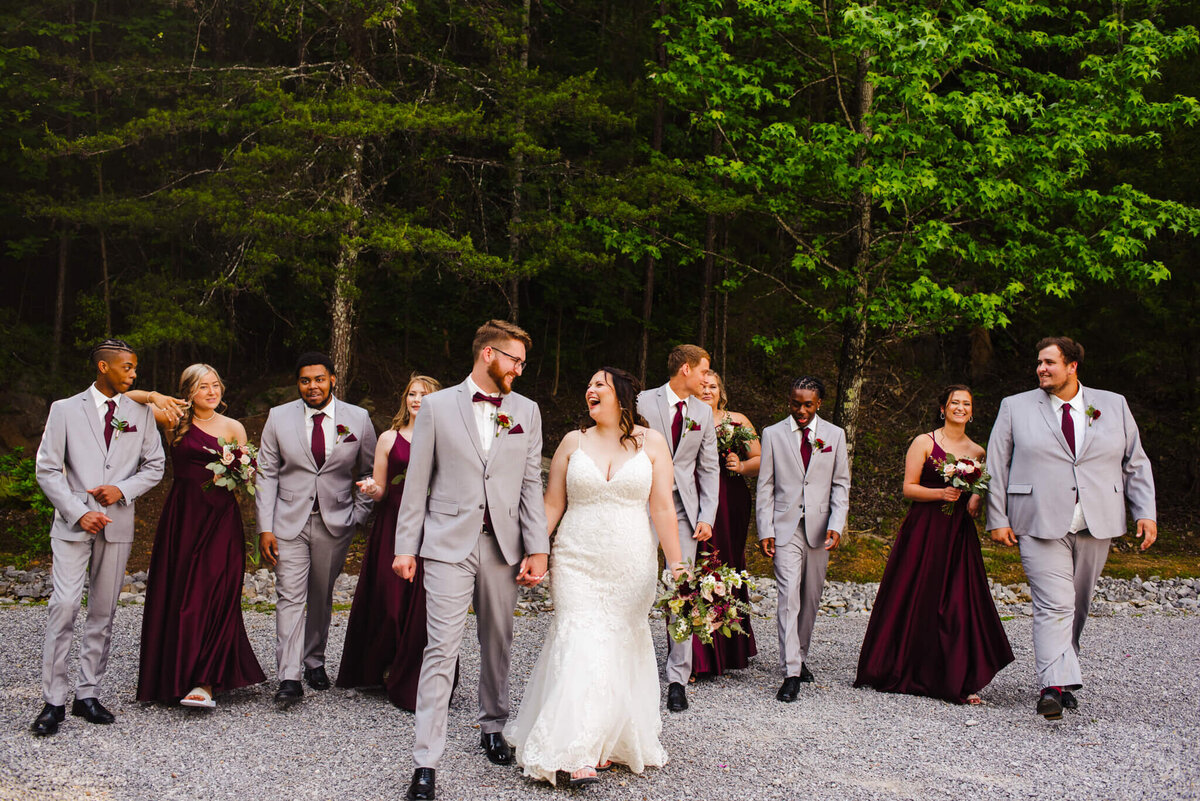 Photo of a bride and groom holding hands and walking while their wedding party follows in the background
