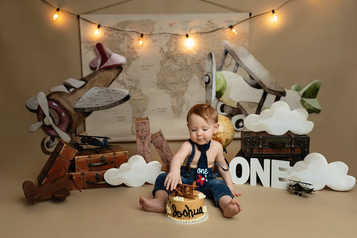A toddler boy reaches for a cake to celebrate his first birthday in a studio
