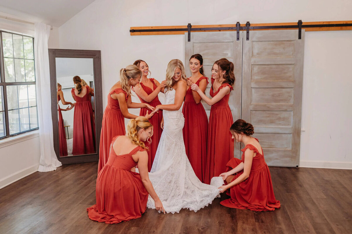 photo of a bride as a her bridesmaid surround her and adjust her dress