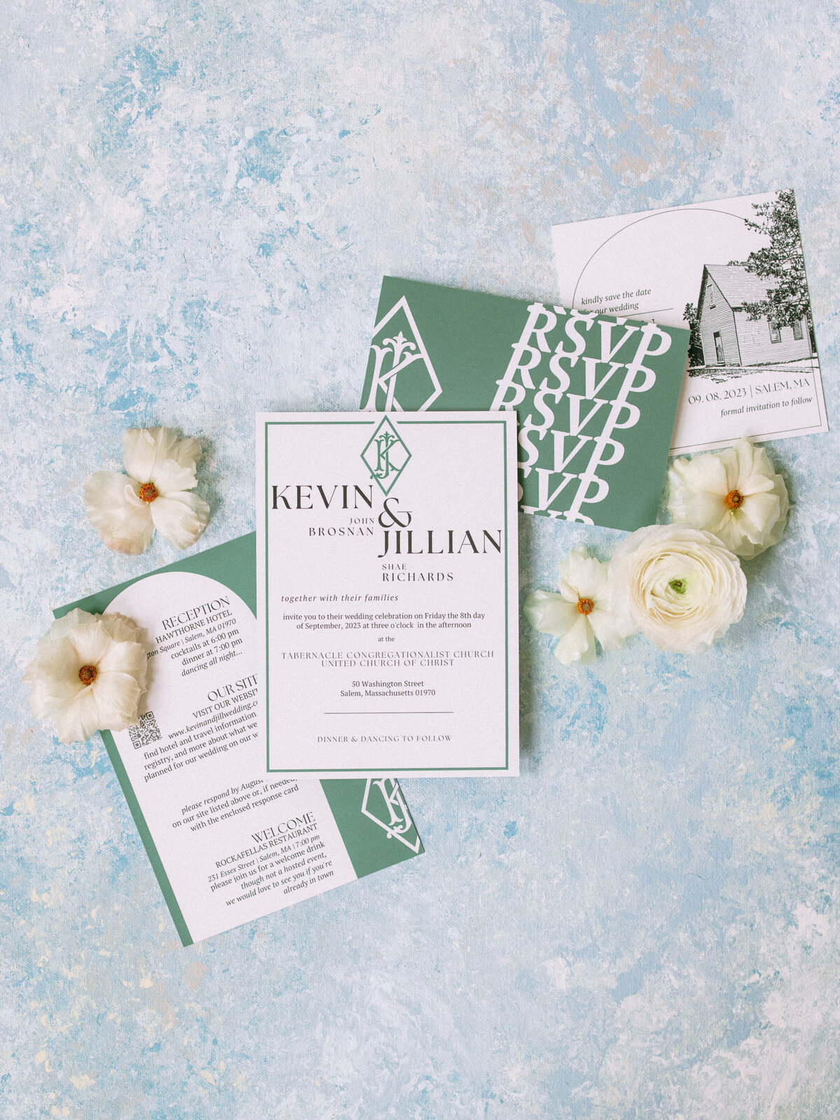 Flat lay of green and white wedding invitation suite on a blue patterned background with white flowers