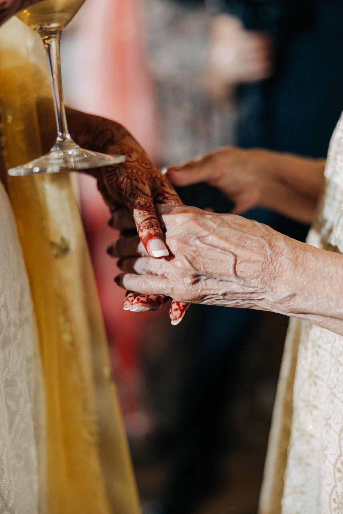 A close-up of a young woman's hand with henna tattoos touching an elderly woman's hand during a cultural event.