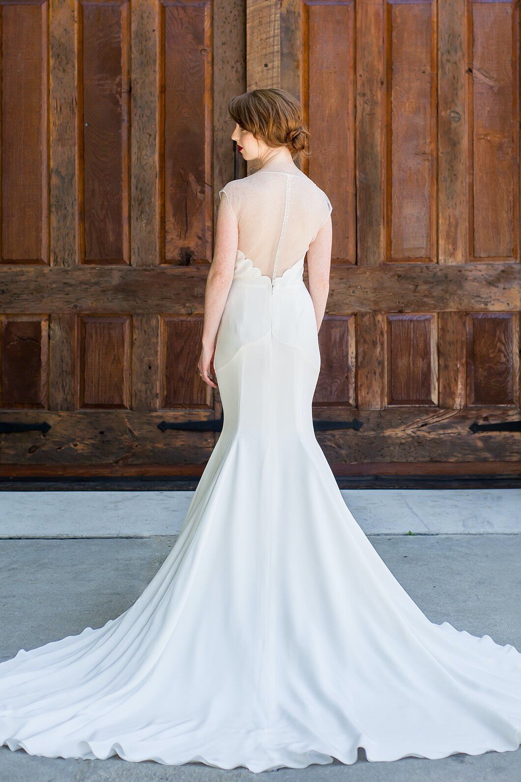 The mermaid silhouette of this crepe wedding gown is emphasized by the dramatic cathedral train and the illusion back bodice that points down to it.