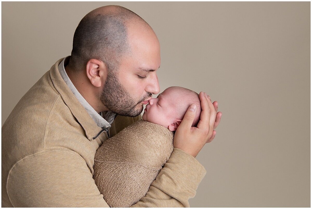 Close up image of Dad holding his swaddled baby boy and kissing his nose.