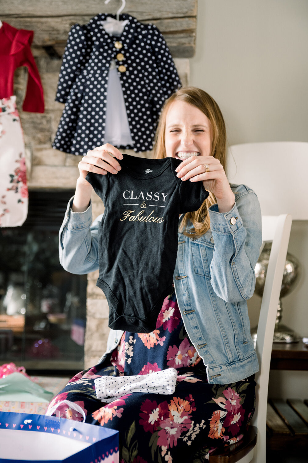 Mom-to-be proudly holding up a onesie with the phrase 'Classy and Fabulous' at a pink and yellow girl baby shower.