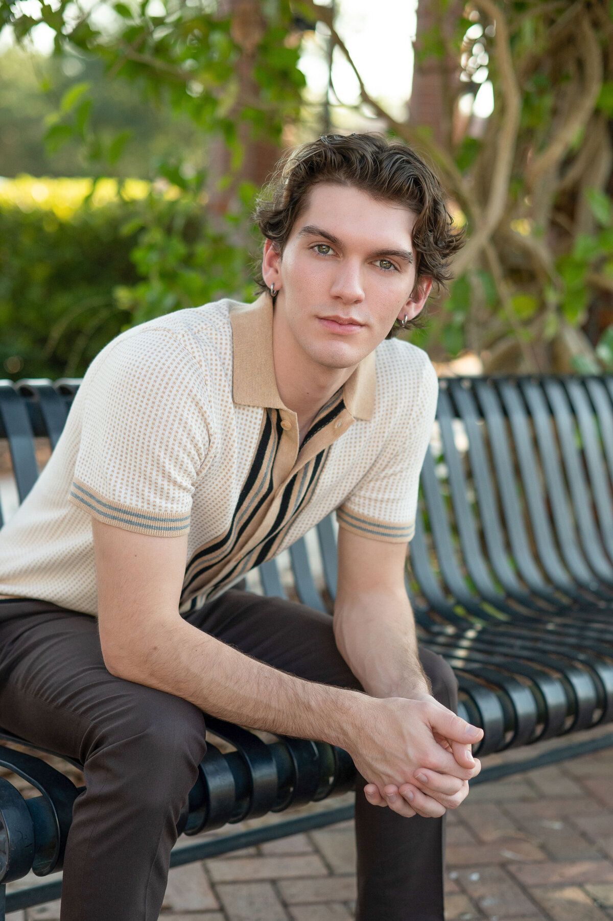 High school senior boy sitting on bench looking at camera with a serious expression.