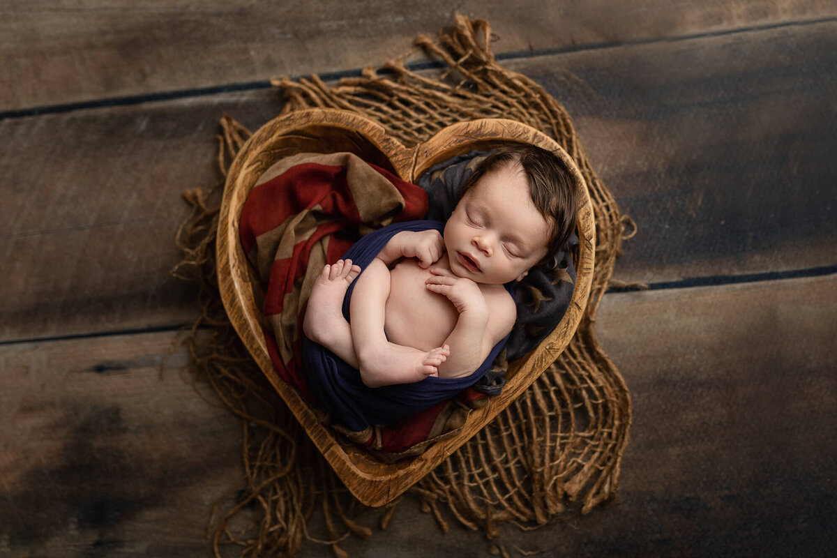 Newborn boy in a wooden heart bowl.