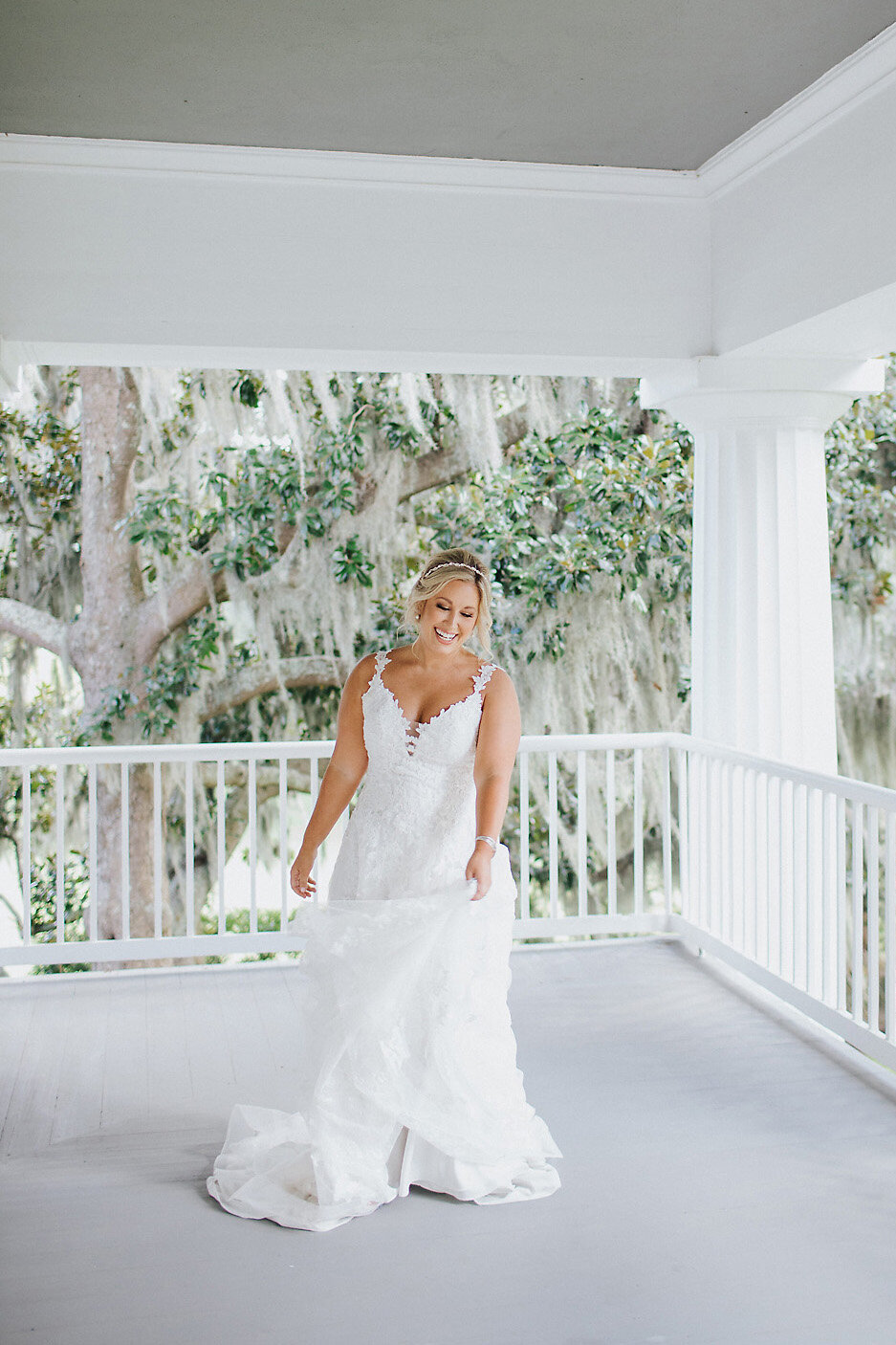 Bride standing on porch with oaks behind her.