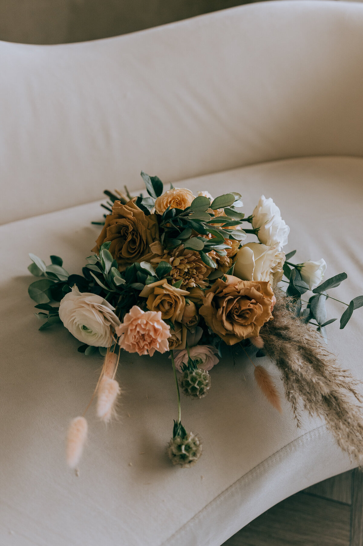 A bouquet of flowers with roses and greenery rests on a beige sofa.