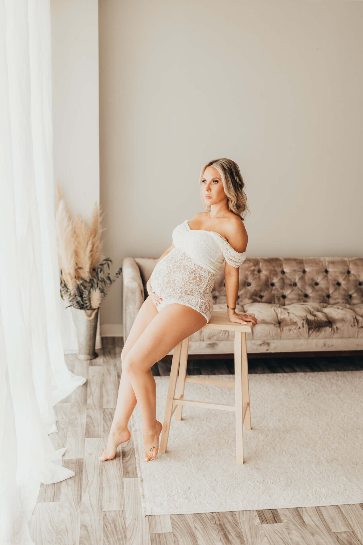 pregnant mom leans on pine stool in front of window in studio for ally's photography