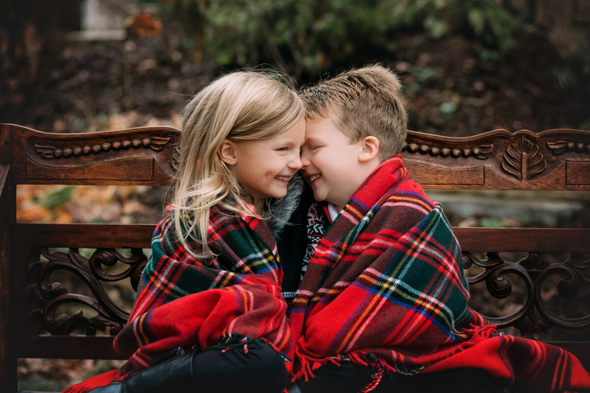 boy and girl snuggling under plaid blanket on bench